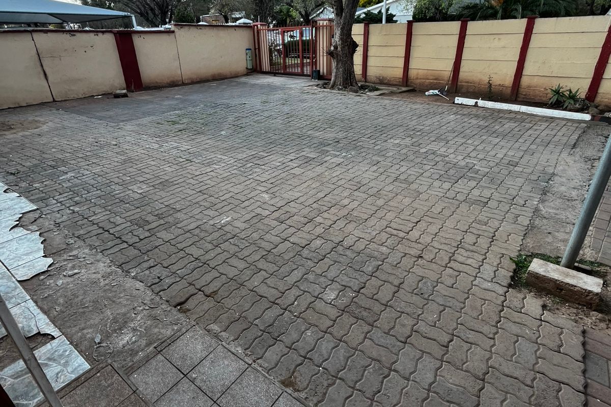 A spacious paved rear courtyard featuring a perimeter wall, metal gate access, and a tiled patio area in need of maintenance.