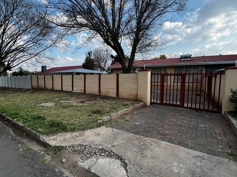 Front exterior view of the property featuring a paved driveway, secure metal gate, perimeter wall, and a corrugated metal roof with solar geyser.