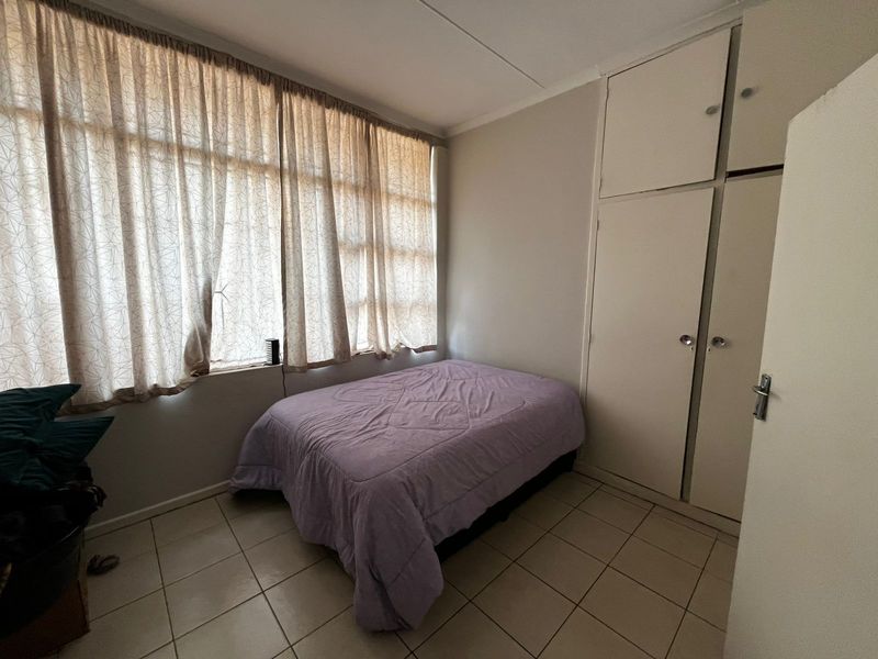 A functional bedroom featuring built-in cupboards, tiled flooring, and large windows with curtain rails, offering a neutral base for personalization.
