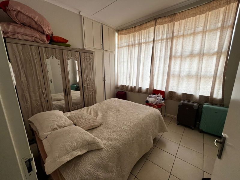 A bedroom featuring tiled flooring, large windows with curtains, and built-in cupboards providing ample storage space.