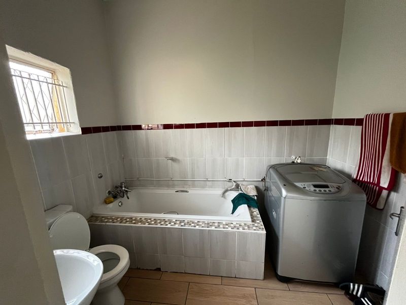 A functional bathroom featuring a built-in bathtub, toilet, and tiled finishes, with space for laundry appliances.