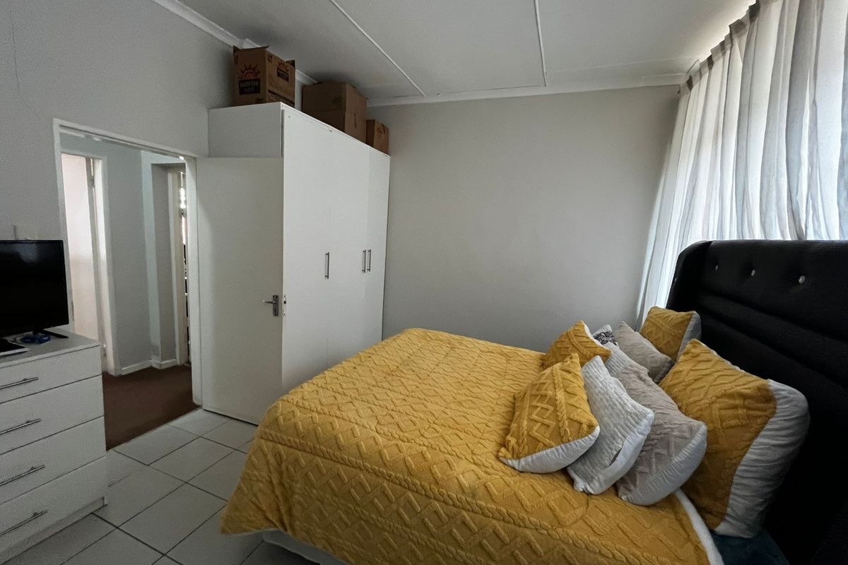 A functional bedroom featuring tiled flooring, a built-in wardrobe, and large windows with curtains, offering a clean and practical living space.