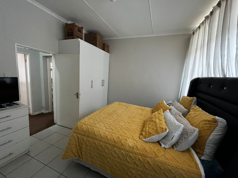A functional bedroom featuring tiled flooring, a built-in wardrobe, and large windows with curtains, offering a clean and practical living space.