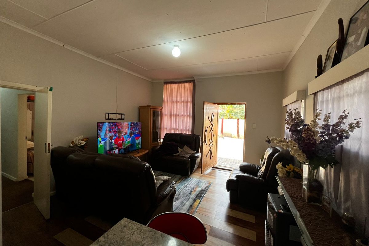 A living room featuring tiled flooring and direct access to the exterior through a timber door, with visible ceiling finishes.