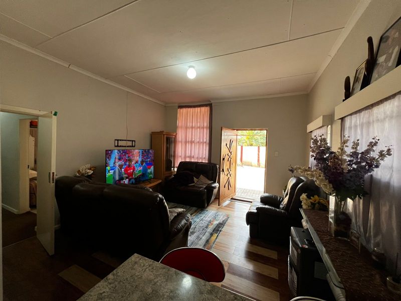 A living room featuring tiled flooring and direct access to the exterior through a timber door, with visible ceiling finishes.