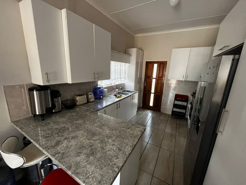 A functional kitchen featuring laminate countertops, white cabinetry, tiled flooring, and a tiled backsplash, providing a practical workspace with direct access to an exterior door.