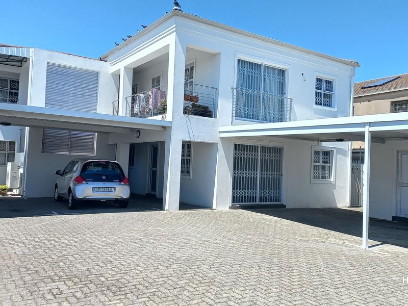 Front view of a multi-level flat featuring a paved driveway, covered carport parking, and a balcony with security gates.