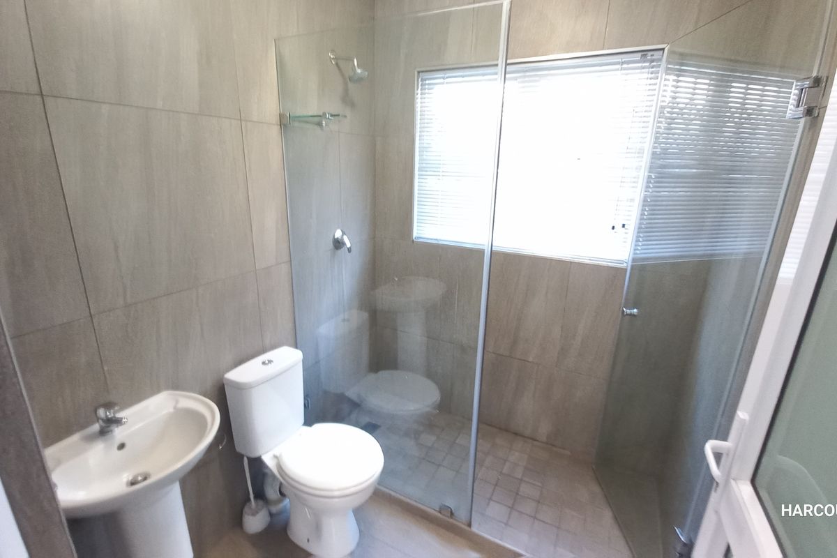 A modern bathroom featuring neutral wall tiles, a pedestal basin, a toilet, and a walk-in shower with a glass screen.