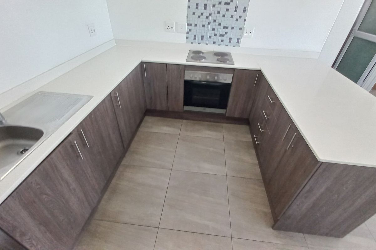 A modern, U-shaped kitchen featuring wood-finish cabinetry, stone countertops, a built-in oven and hob, and neutral tiled flooring.