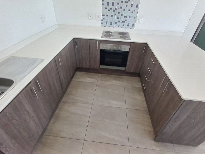 A modern, U-shaped kitchen featuring wood-finish cabinetry, stone countertops, a built-in oven and hob, and neutral tiled flooring.