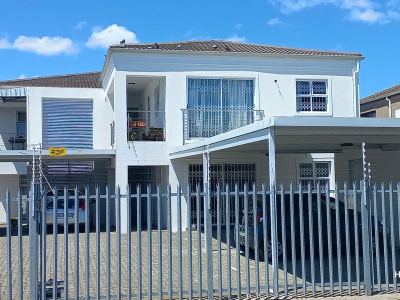 Front elevation of a two-story flat featuring a paved driveway, carport, metal security fencing, and balcony access.