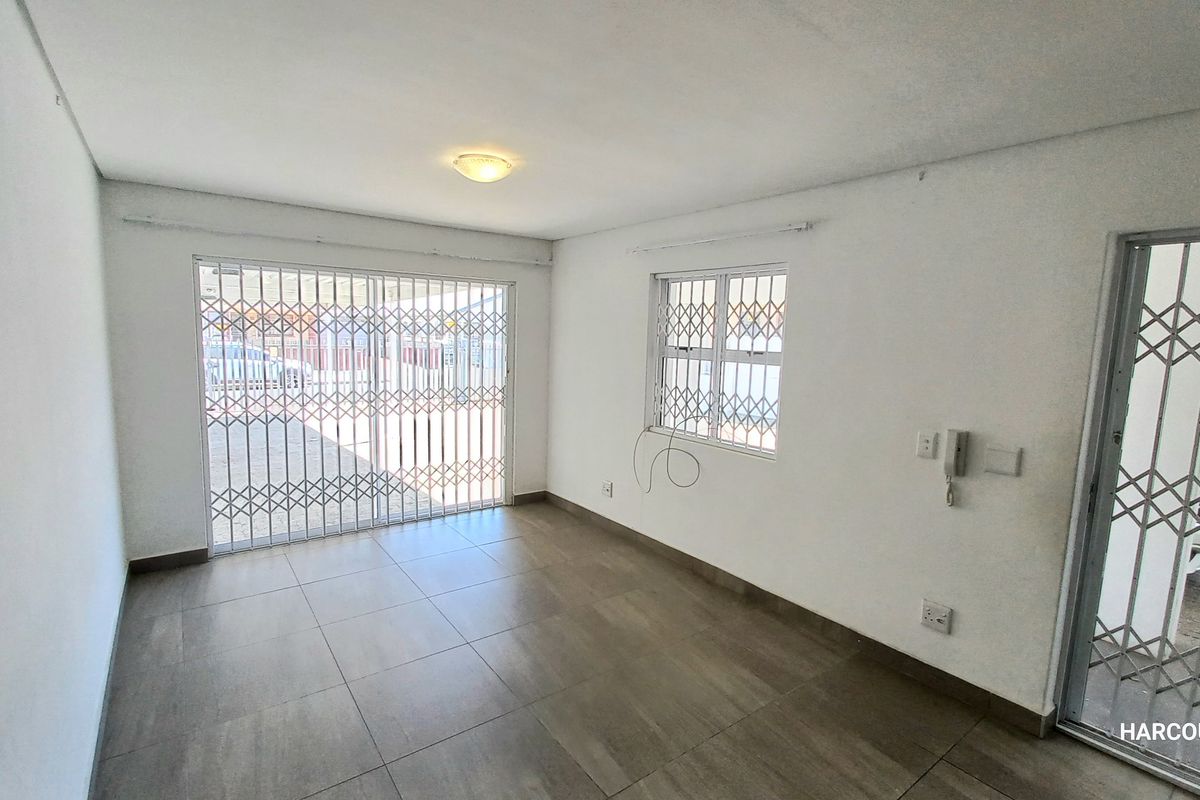 An empty living room featuring tiled flooring, security gates on the windows and doors, and an intercom system.