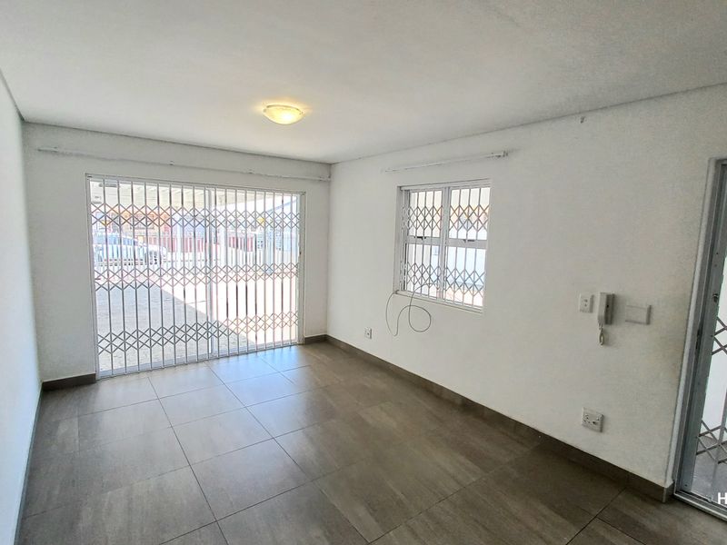 An empty living room featuring tiled flooring, security gates on the windows and doors, and an intercom system.