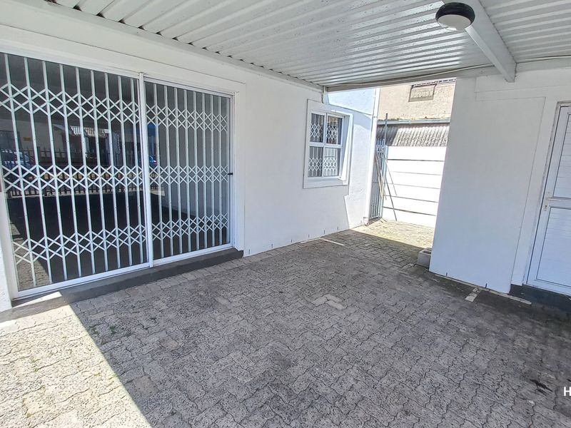 A covered outdoor patio area featuring paved flooring, a corrugated metal roof, and secure sliding door access with fitted security gates.