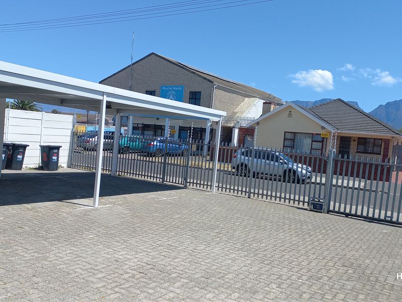 Exterior view of the property featuring a paved driveway, covered carport, and secure metal gate with electric fencing.