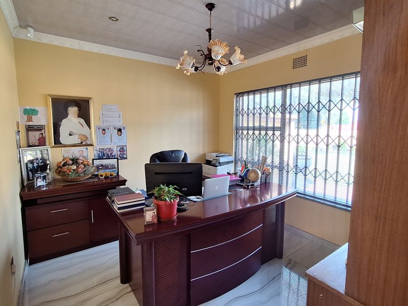 A functional home office space featuring tiled flooring, a large window with security bars, and a central ceiling light fixture.