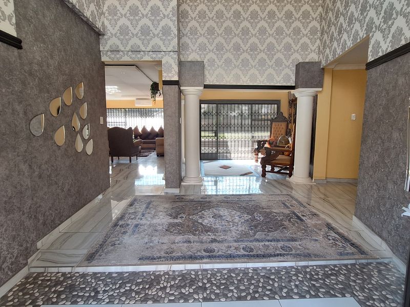 Spacious entrance hall featuring decorative columns, textured wallpaper, and a combination of tiled and pebble inlay flooring leading into the main living area.