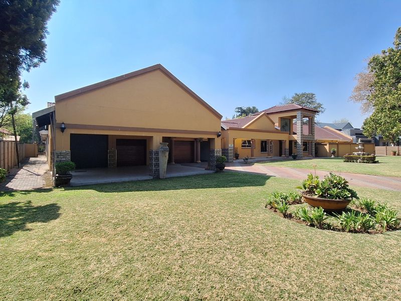 Spacious front exterior view featuring a triple garage, expansive paved driveway, well-maintained lawn, and attractive stone-clad architectural detailing.