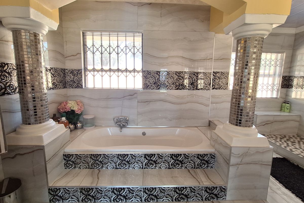 A spacious bathroom featuring a built-in bathtub framed by decorative columns, complemented by modern tiled walls and a separate shower area.