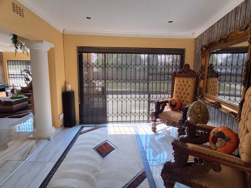 Spacious open-plan living area featuring polished tiled flooring, decorative columns, and large sliding glass doors with integrated security gates for natural light.