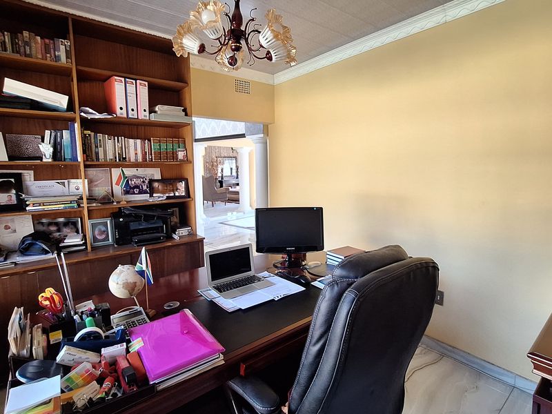 A functional home office featuring extensive built-in wooden shelving, tiled flooring, and decorative ceiling cornice, offering a dedicated workspace.