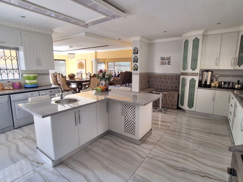 Spacious open-plan kitchen featuring a central island with stone countertops, extensive built-in cabinetry, and modern tiled flooring, seamlessly flowing into the dining area.