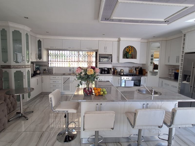 Spacious kitchen featuring a large central island with stone countertops, built-in cabinetry, integrated appliances, and modern tiled flooring with recessed lighting.