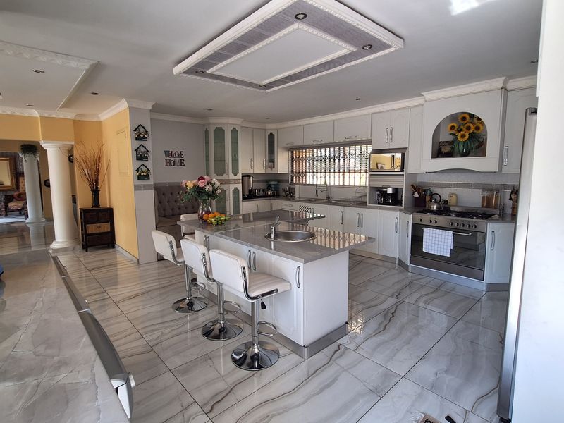 Spacious modern kitchen featuring a central island with sink, stone countertops, built-in oven, gas hob, and elegant tiled flooring throughout.