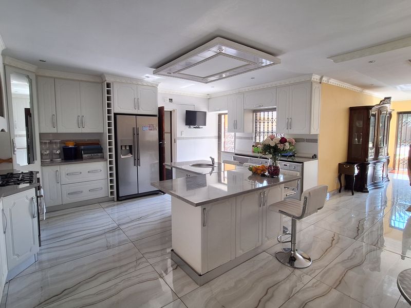 Spacious open-plan kitchen featuring white cabinetry, stone countertops, a central island with a sink, and polished marble-look tiled flooring.