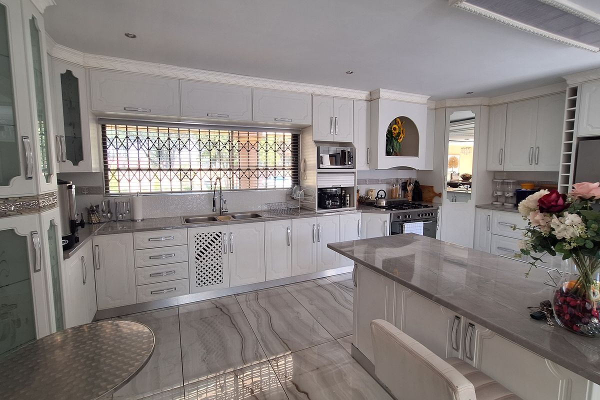 A well-appointed kitchen featuring white cabinetry, stone countertops, a central island, and modern tiled flooring with a large window protected by a security gate.