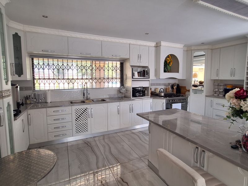A well-appointed kitchen featuring white cabinetry, stone countertops, a central island, and modern tiled flooring with a large window protected by a security gate.