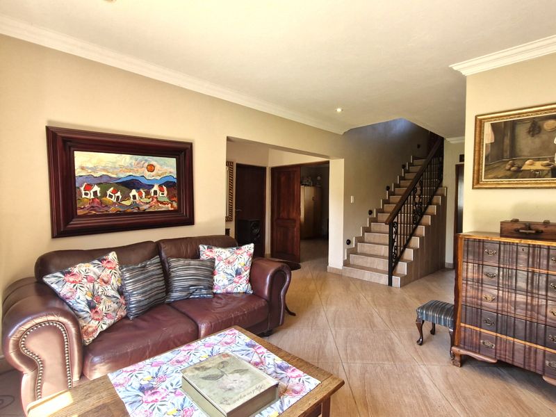A well-maintained living room featuring tiled flooring, coved cornicing, and a staircase with a decorative wrought iron balustrade leading to the upper level.