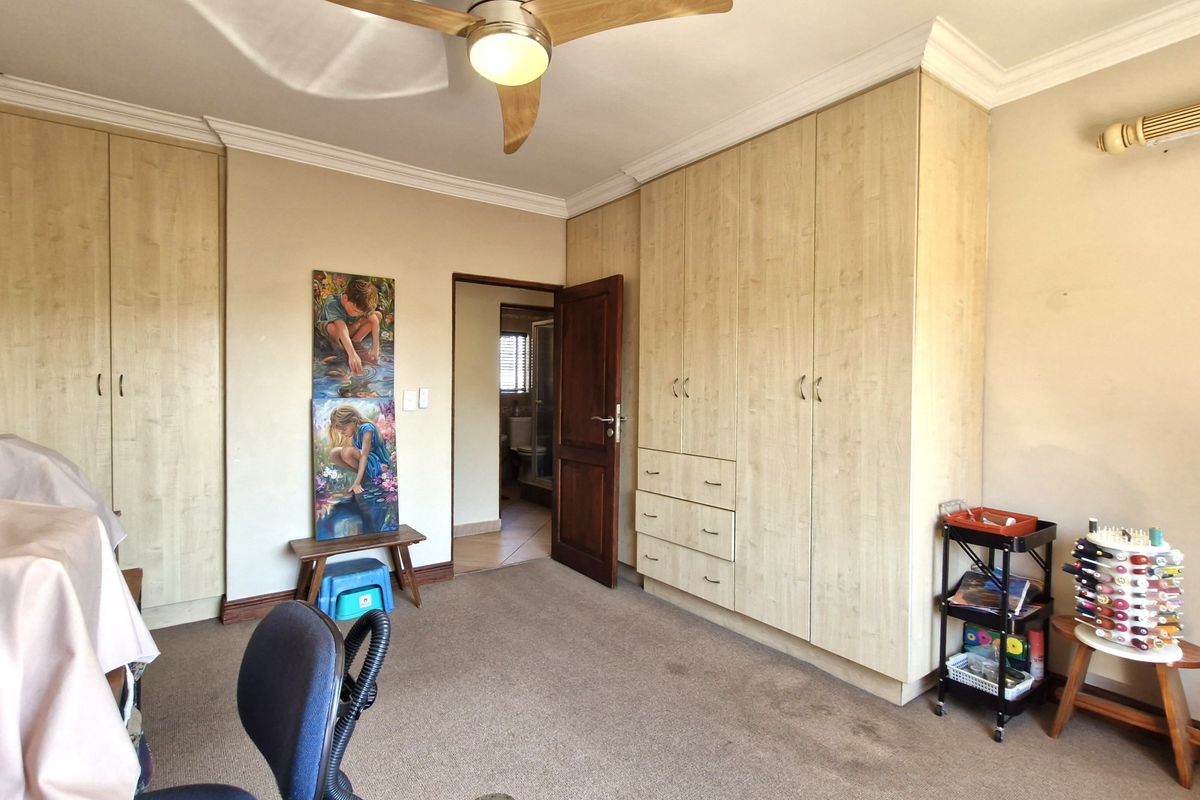 A bedroom featuring extensive built-in cabinetry, carpeted flooring, and a ceiling fan, with an adjoining en-suite bathroom visible through the doorway.