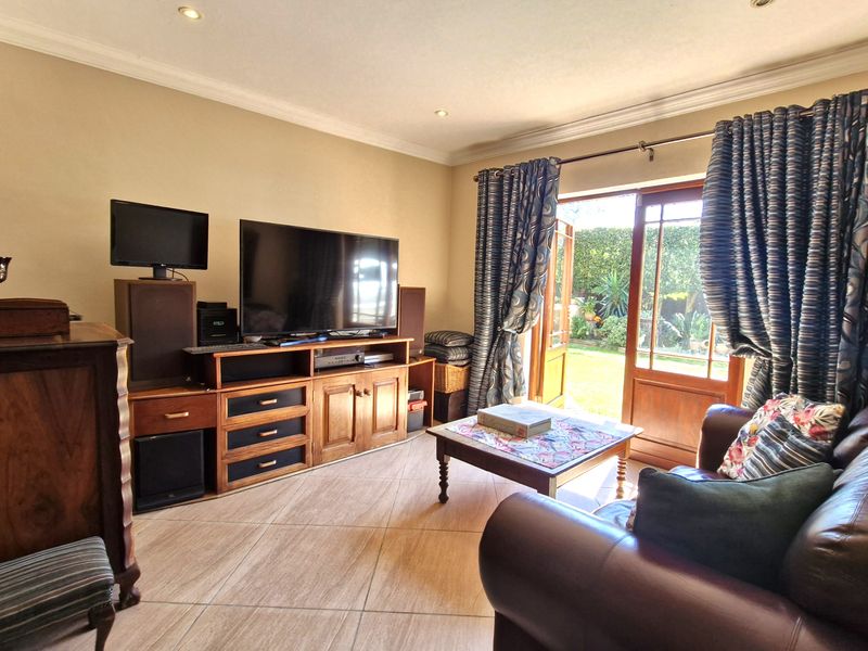 A comfortable living room featuring tiled flooring, recessed downlighting, and direct access to the rear garden through timber-framed glass doors.