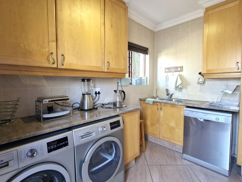 Functional scullery featuring light wood cabinetry, granite countertops, tiled backsplash, and dedicated space for laundry appliances and a dishwasher.