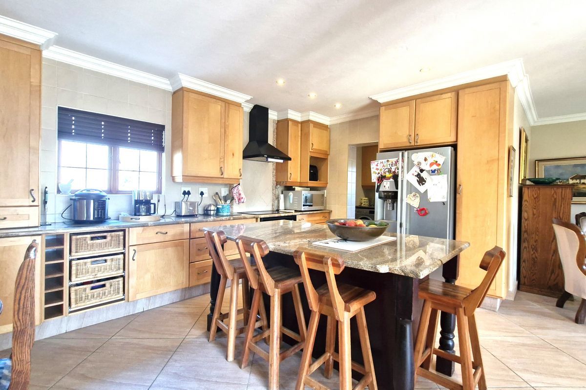 A spacious kitchen featuring wooden cabinetry, granite countertops, a central island with seating, and tiled flooring.