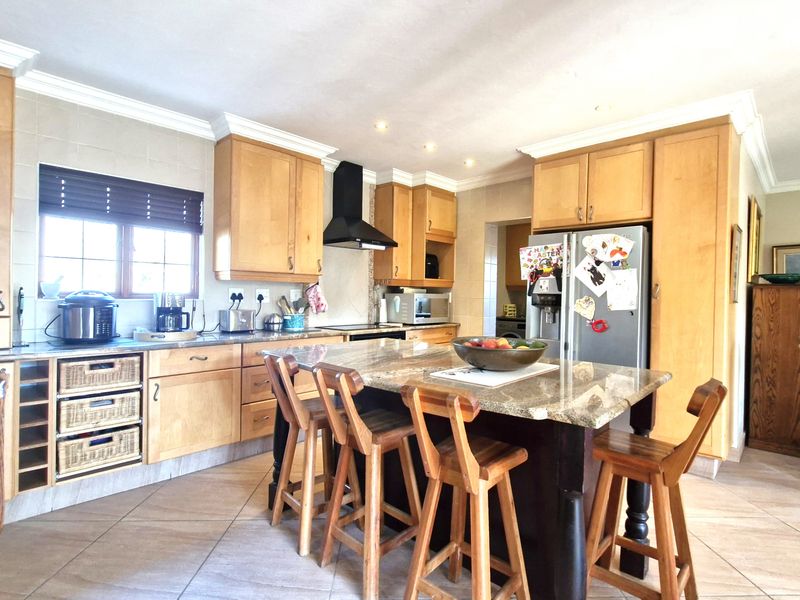 A spacious kitchen featuring wooden cabinetry, granite countertops, a central island with seating, and tiled flooring.
