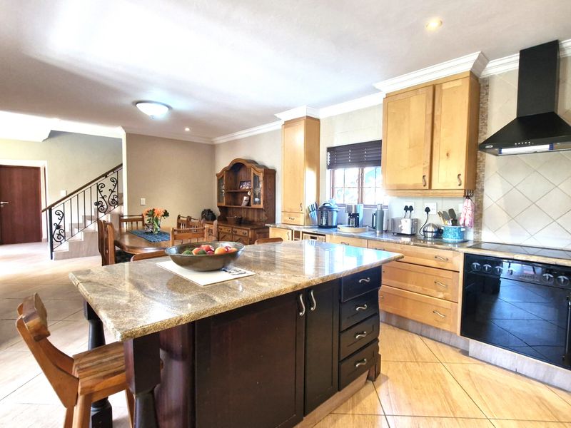 Spacious open-plan kitchen and dining area featuring a central island, granite countertops, wooden cabinetry, and a staircase with decorative wrought iron railings.