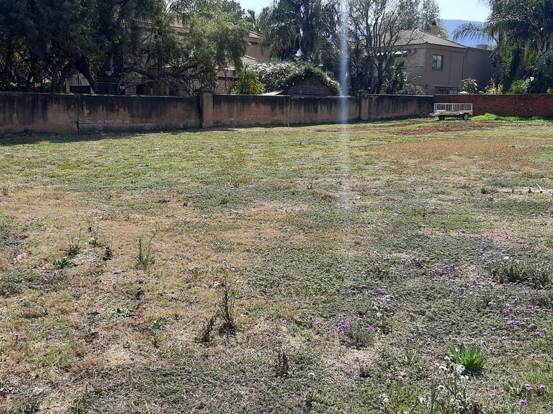 A vacant residential plot featuring a grass lawn and a perimeter boundary wall.