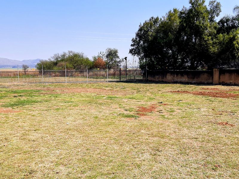 A spacious, level residential plot featuring established perimeter fencing, boundary walls, and mature trees, offering a clear canvas for future development.