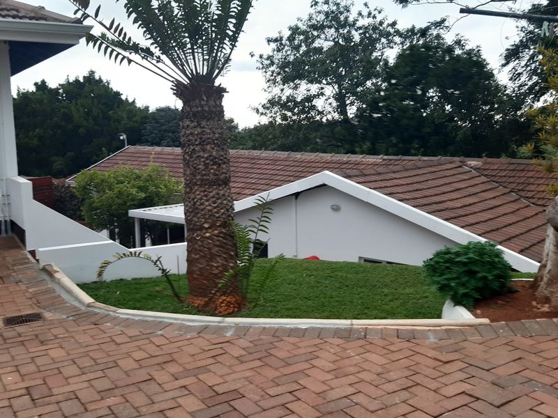 Rear exterior view of the cottage featuring a brick paved driveway, landscaped lawn, and tiled roof structure.