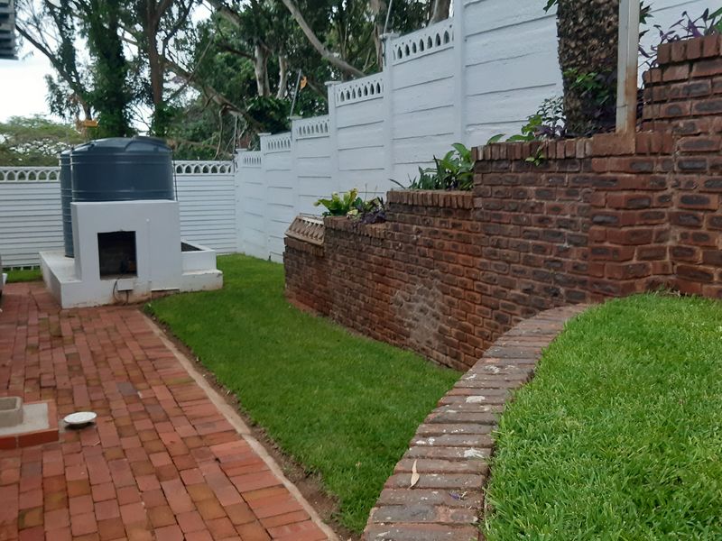 Rear garden area featuring tiered brick retaining walls, brick paved pathways, a water tank, and a white precast boundary wall.