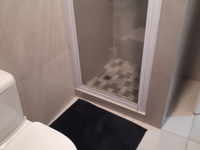 A clean, modern bathroom featuring a white toilet and a glass-enclosed shower with neutral-toned wall and floor tiling.