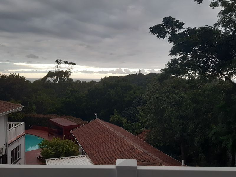 Elevated view overlooking the property's swimming pool, surrounding garden, and distant landscape under a cloudy sky.