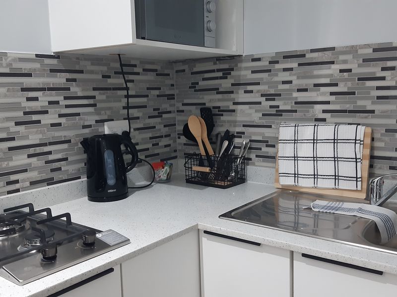A modern kitchen corner featuring a gas hob, built-in microwave, stone countertops, and a stainless steel sink with a tiled backsplash.
