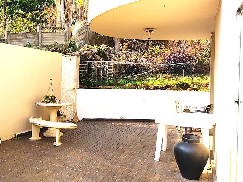 A covered outdoor patio area featuring brick paving and a retaining wall, providing a functional space for outdoor relaxation.