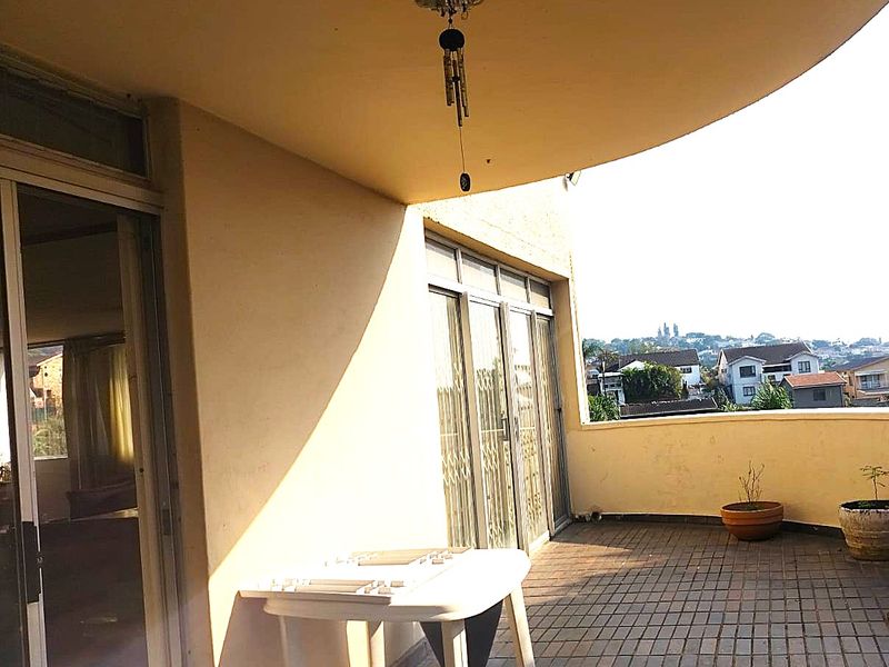 A spacious covered balcony featuring tiled flooring, sliding glass door access, and elevated views of the surrounding neighborhood.