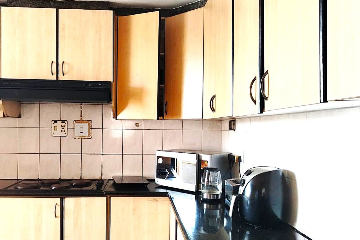 A functional kitchen featuring light wood-finish cabinetry, black granite countertops, a built-in electric hob, and a tiled backsplash.