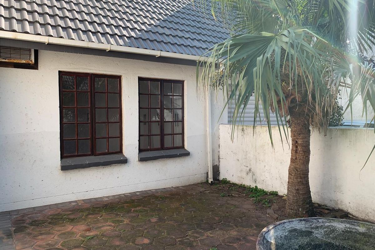 Rear courtyard area featuring paved flooring, timber-framed windows, and a tiled roof section, requiring maintenance to address moss and weathered finishes.