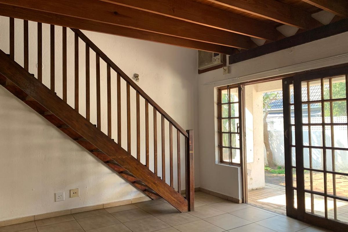 Open plan living area featuring exposed wooden ceiling beams, a wooden staircase, tiled flooring, and direct access to an outdoor patio through sliding doors.